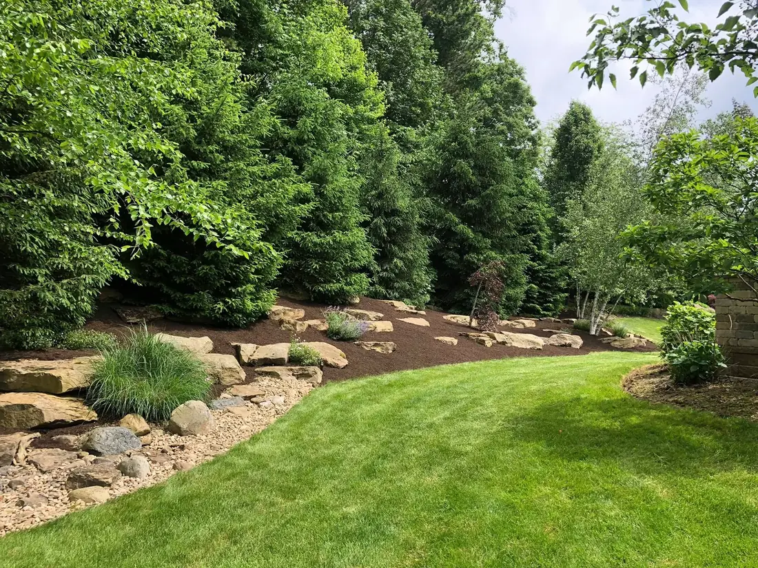 Finished backyard landscape bed with boulders, mulch, trees, and lawn by Going Yard
